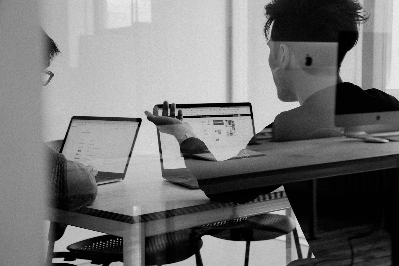 Two people at a strategy table, work reviewed through glass.